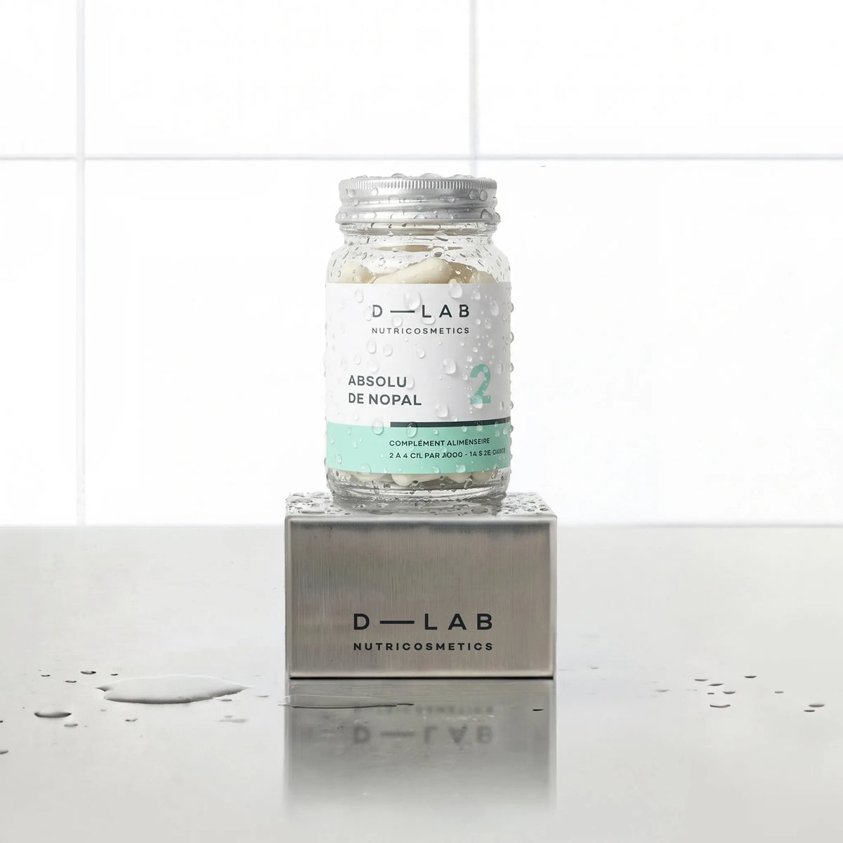 Absolu de Nopal D-LAB Nutricosmetics, cure 1 mois : flacon en verre de gélules posé sur un socle inox brossé, fond carrelage blanc