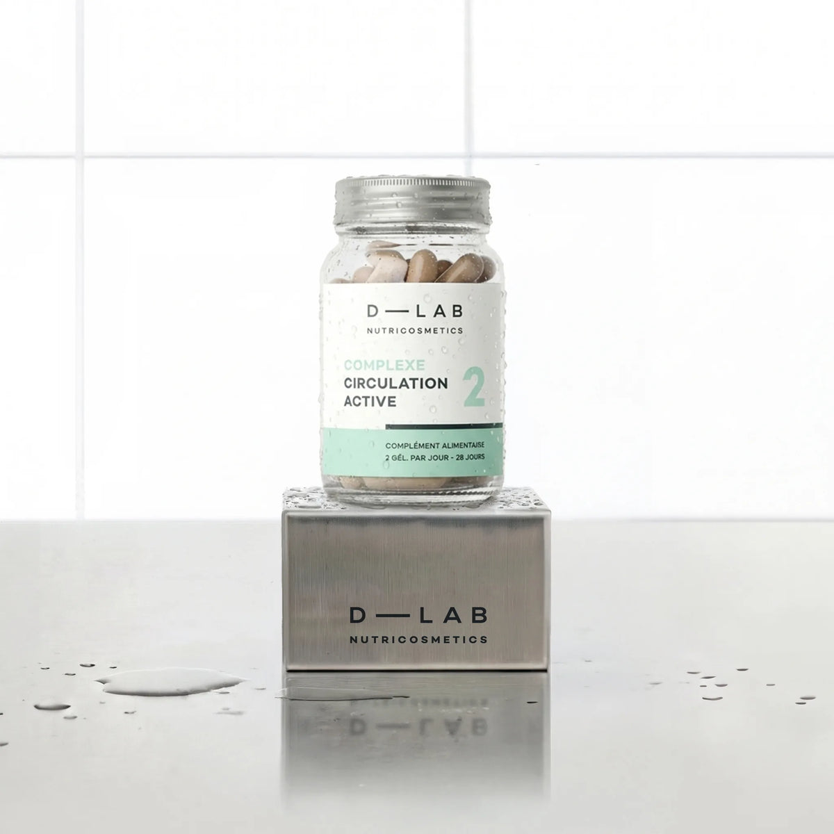 Complexe Circulation Active D-LAB Nutricosmetics, cure 1 mois : flacon en verre de gélules posé sur un socle inox brossé, fond carrelage blanc
